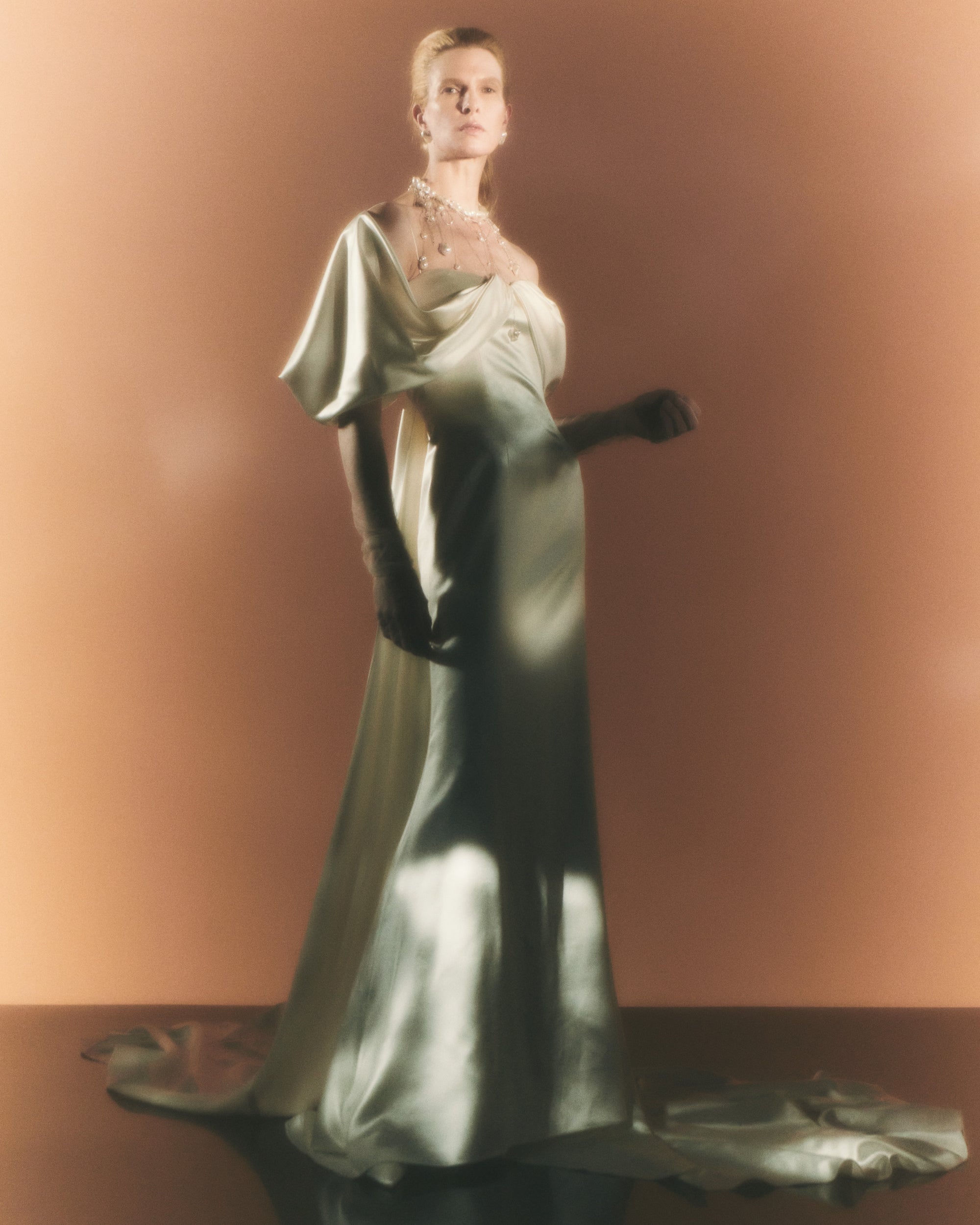 Silk wool gown with asymmetrical swagged sleeve. Detachable watteau train pouring down center back. External darts for shaping and spaghetti straps for contrast. Soft internal bustier with side boning, cups, and grosgrain belt with 3 hook position. Low center back zip, hook and eye closure.
