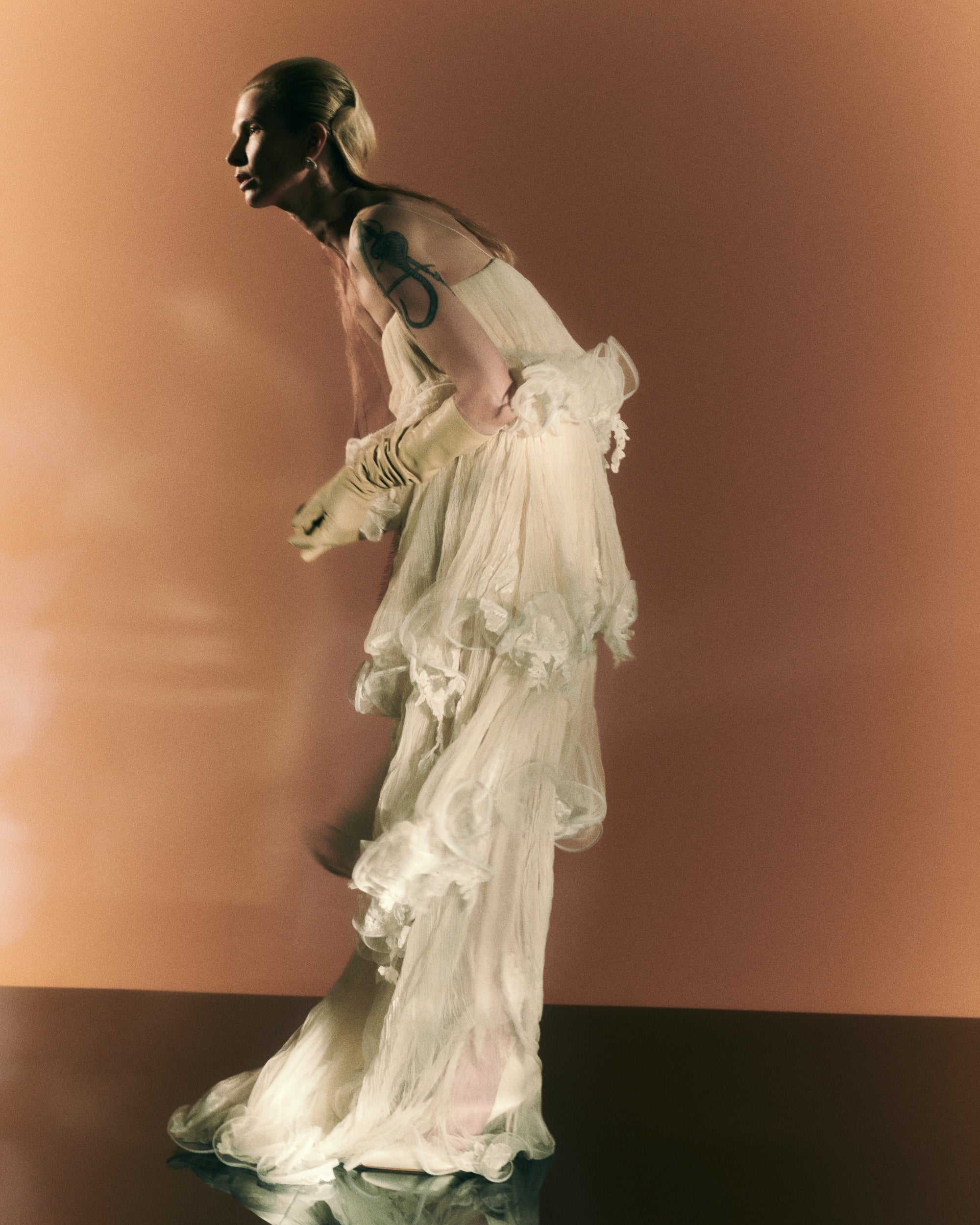 Tiered tulle gown with hand appliquéd chantilly and corded lace. Four layered tulle body pronounced by delicate horsehair edge. Below knee lining for slight transparency at calf. Soft square neckline with spaghetti strap. Free of cups and boning and finished with center back zip close.